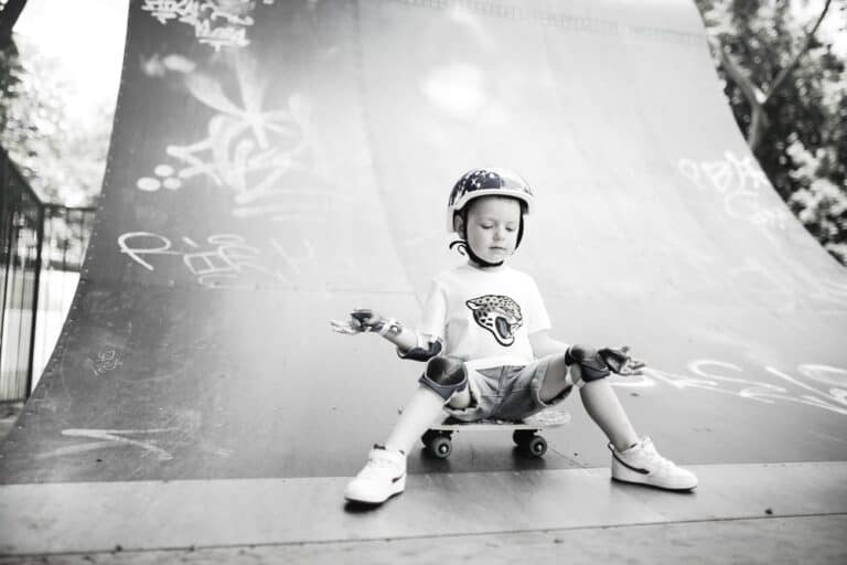 young boy sitting on skateboard at bottom of skate ramp