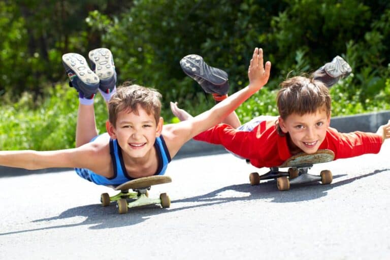 two boys lying on their skate boards rolling down the road having fun