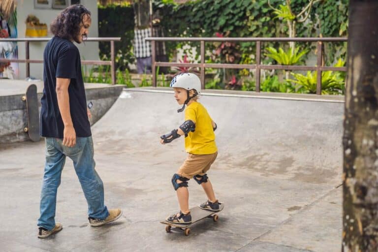 boy learning to skateboard with father on skateboard ramp
