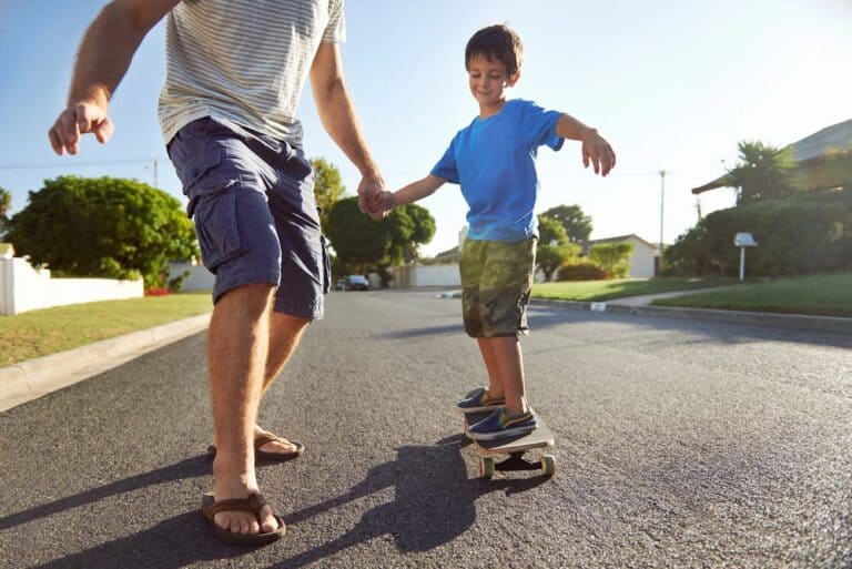 father helping young boy to learn how to skateboard